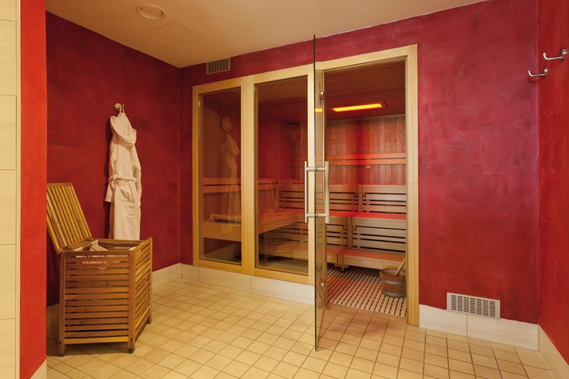 Moderner Saunaraum mit Holzinterieur Innenansicht eines Saunaraums mit gläserner Tür, Holzbank und roter Wand. Ein Bademantel hängt an der Wand.