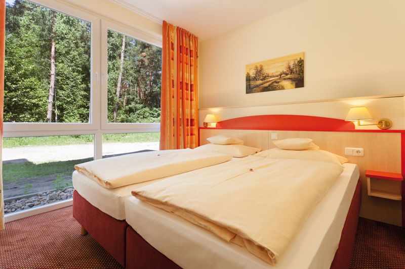 Gemütliches Hotelzimmer mit Blick ins Grüne Helles Hotelzimmer mit zwei nebeneinander stehenden Einzelbetten, großen Fenstern mit Ausblick ins Grüne, und einer Wanddekoration.